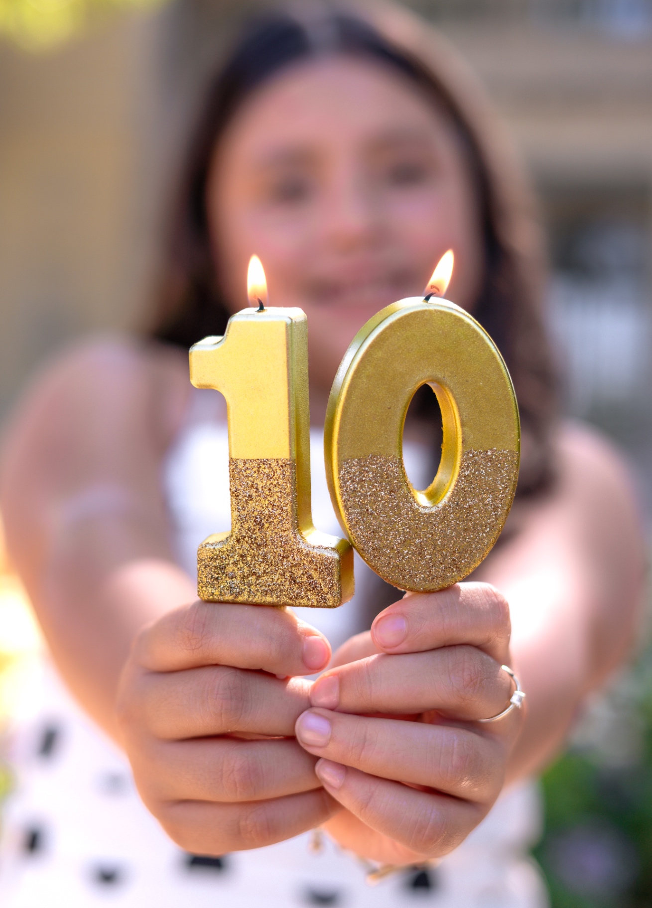 A girl holding two lit gold number candles forming a ten toward the camera.