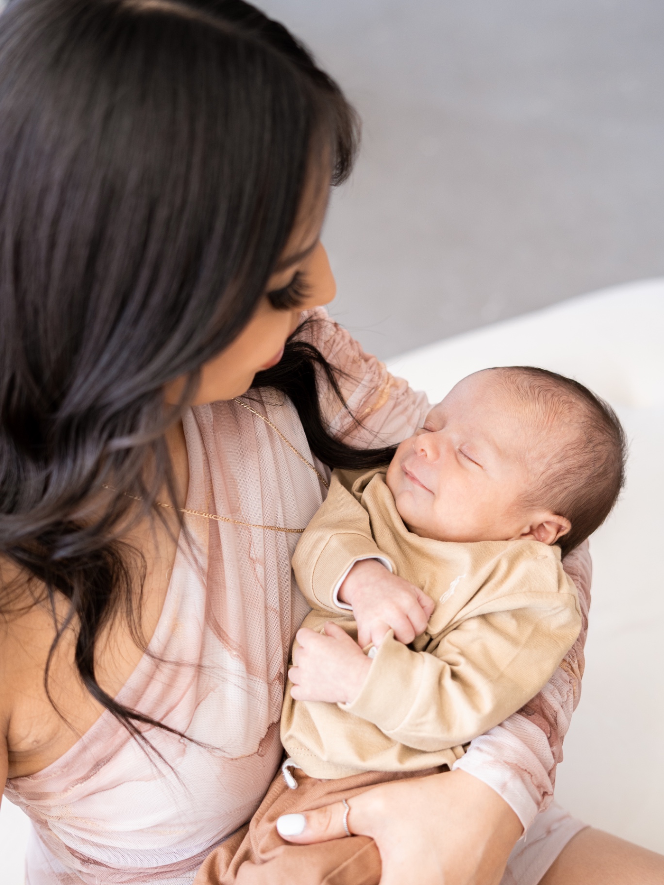 A mother holding a sleeping newborn in a soft neutral studio.